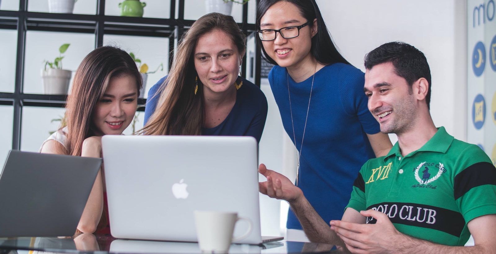 four people watching on white MacBook on top of glass-top table